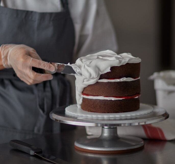 Baker frosting a 3 layer chocolate cake with white icing