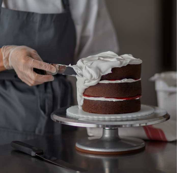 Baker frosting a 3 layer chocolate cake with white icing